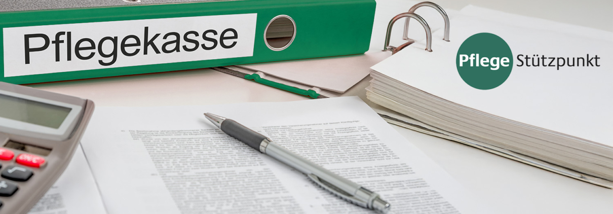 Ordner mit der Aufschrift „Pflegekasse“, Unterlagen und ein Stift auf einem Schreibtisch.