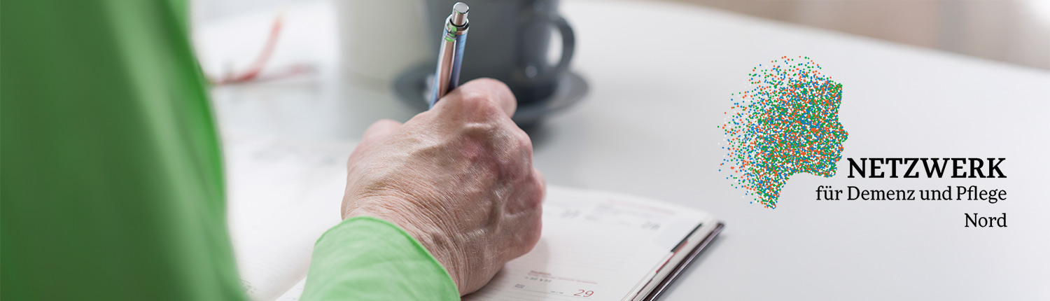 Ältere Person sitzt am Tisch und macht sich Notizen in einem Kalender.