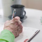 Ältere Person sitzt am Tisch und macht sich Notizen in einem Kalender.